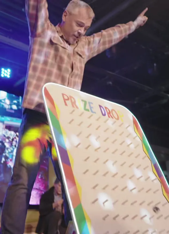 A guest celebrating on stage next to a giant prize board game