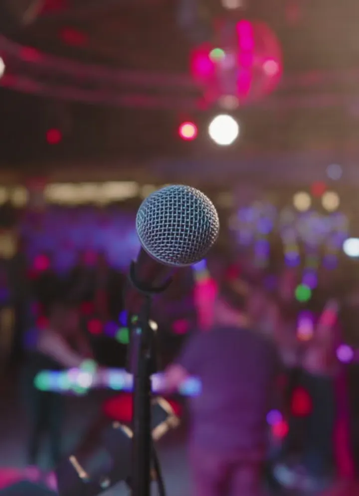 A microphone on stage in front of a crowd under pink party lights
